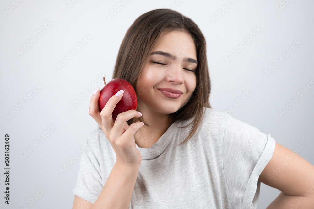 young brunette seductive woman holding red apple in her hand near her face standing on isolated white background dietology and nutrition young brunette seductive woman holding red apple in her hand near her face standing on isolated white background dietology and nutrition
