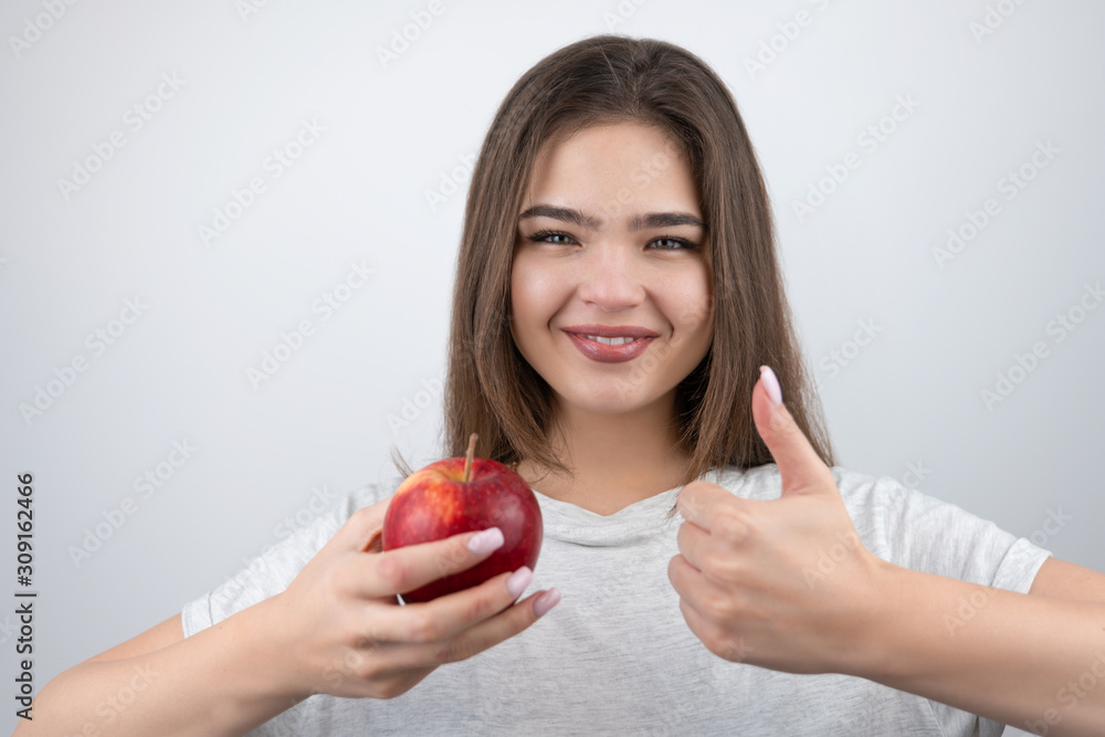 young brunette seductive woman holding red apple in her hand showing like sign standing on isolated white background dietology and nutrition young brunette seductive woman holding red apple in her hand showing like sign standing on isolated white background dietology and nutrition