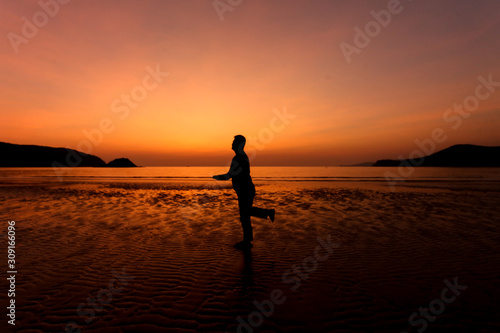 Silhouette action of a young man fun under twilight sunset sky at sea beach. © Taweesak