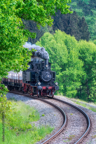 Alte Dampflok mit Waggons in einer Kurve vor Bäumen.