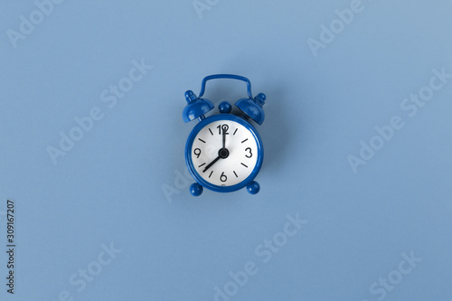 Small alarm clock on pastel background in Classic Blue colour, close-up, top view. Minimal retro style. Time management, Color of the year 2020 concept. Copy space for text. Horizontal orientation