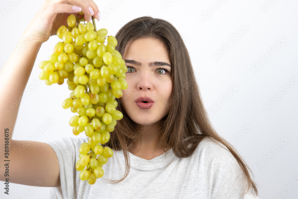 young beautiful surprised woman standing with bunch of green grapes standing on isolated white background dietology and nutrition young beautiful surprised woman standing with bunch of green grapes standing on isolated white background dietology and nutrition