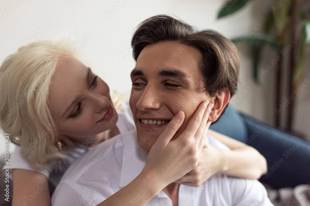 Smiling blonde girl touching boyfriend face at home Smiling blonde girl touching boyfriend face at home
