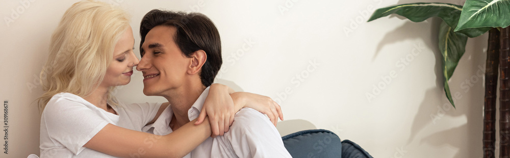 Side view of smiling couple embracing on sofa in living room, panoramic shot Side view of smiling couple embracing on sofa in living room, panoramic shot