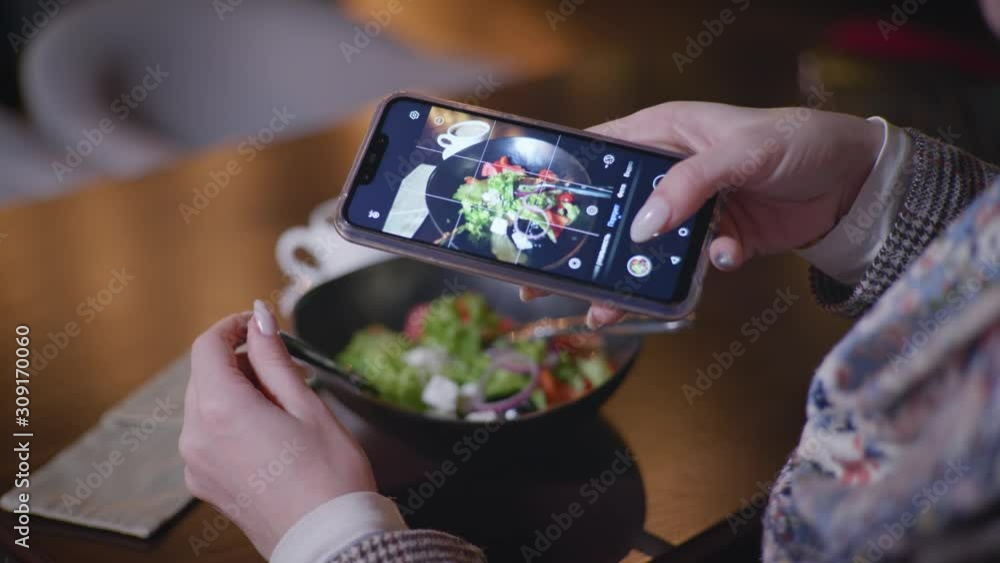 food photographer, fashion blogger takes pictures of vegetable salad on his smartphone for his social media account while sitting at a table in a trendy cafe food photographer, fashion blogger takes pictures of vegetable salad on his smartphone for his social media account while sitting at a table in a trendy cafe