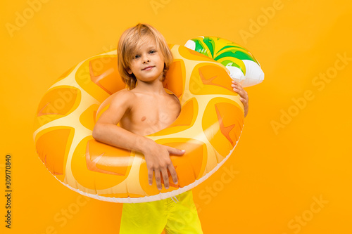 european blond boy in yellow swimming trunks with swimming circle pineapple on an orange background photo