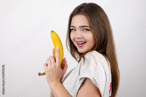 young attractive woman holding banana like a gun in her hand looking sexy standing on isolated white background dietology and nutrition