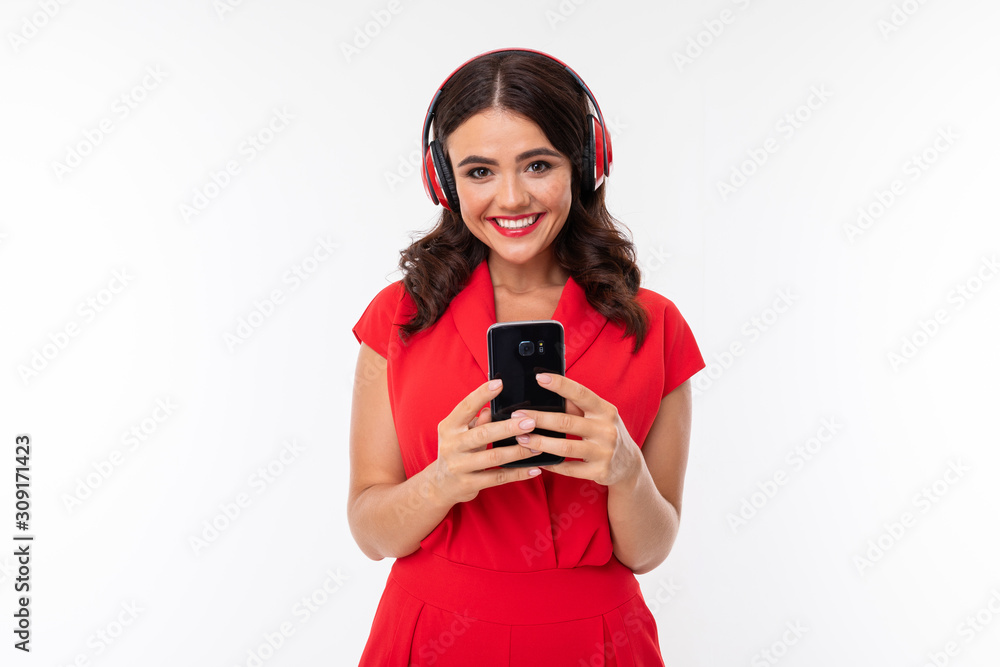 smiling brunette girl in a red dress in headphones with a telephone on a white background smiling brunette girl in a red dress in headphones with a telephone on a white background