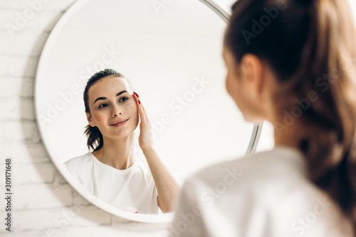 The woman is making up in the bathroom. Woman in bathroom applying cream on face.