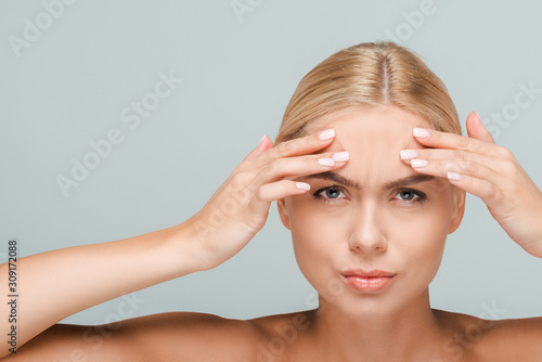 young and naked woman touching forehead isolated on grey