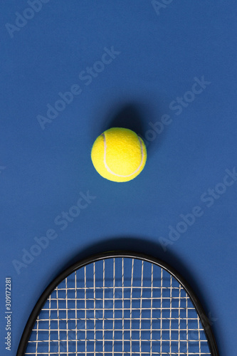 Yellow tennis ball and black racket on blue background. Color of the year 2020, vertical format photo. Active lifestyle concept. Sports equipment, above © Olha Kozachenko