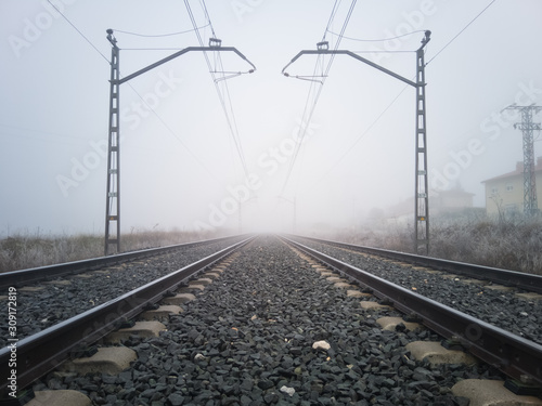 Train tracks and catenary posts disappear into thick fog photo