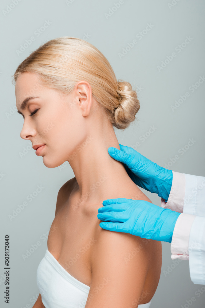 cropped view of beautician in blue latex gloves touching neck of woman with closed eyes isolated on grey