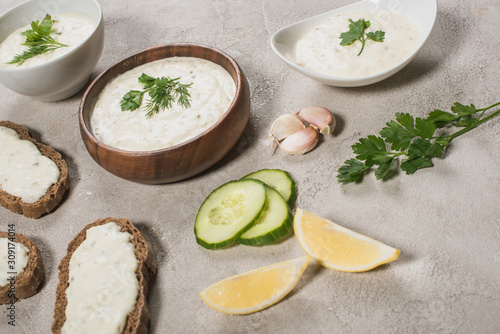 Homemade tzatziki sauce in bowls with fresh ingredients on stone surface