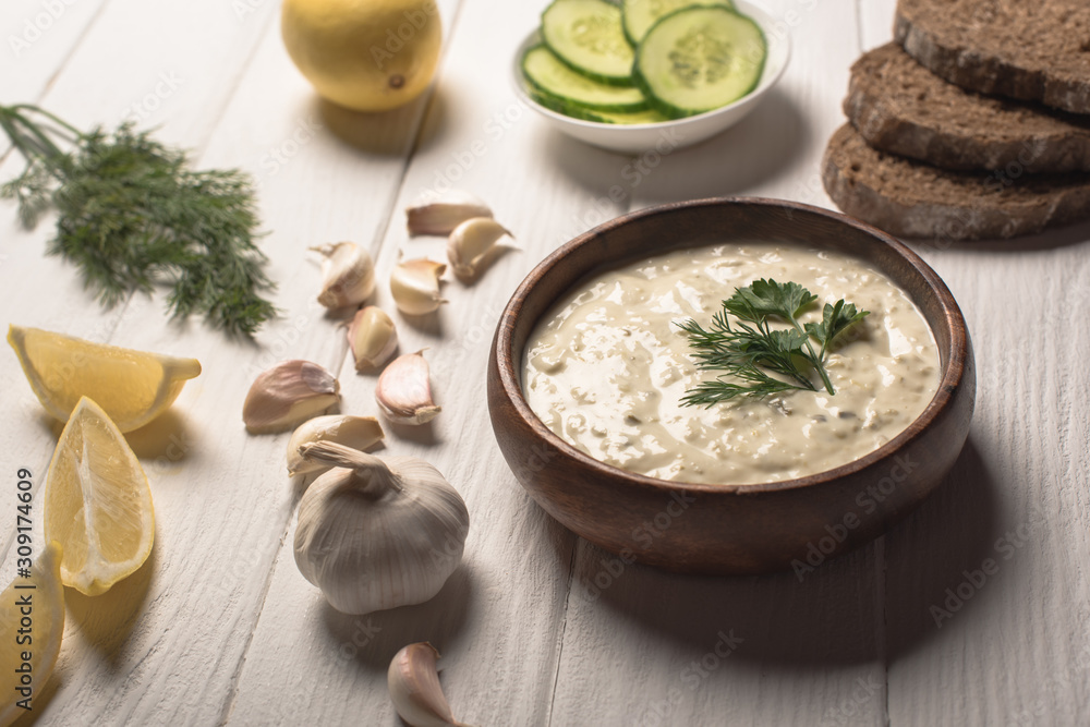 Tzatziki sauce in wooden bowl with ingredients on white wooden background Tzatziki sauce in wooden bowl with ingredients on white wooden background