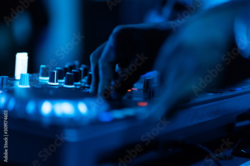 club dj plays music on stage in nightclub.Hand of disc jockey adjusting sound track volume level.Professional audio equipment on music festival