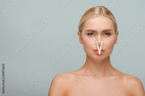 beautiful and naked young woman with wooden pin on nose isolated on grey