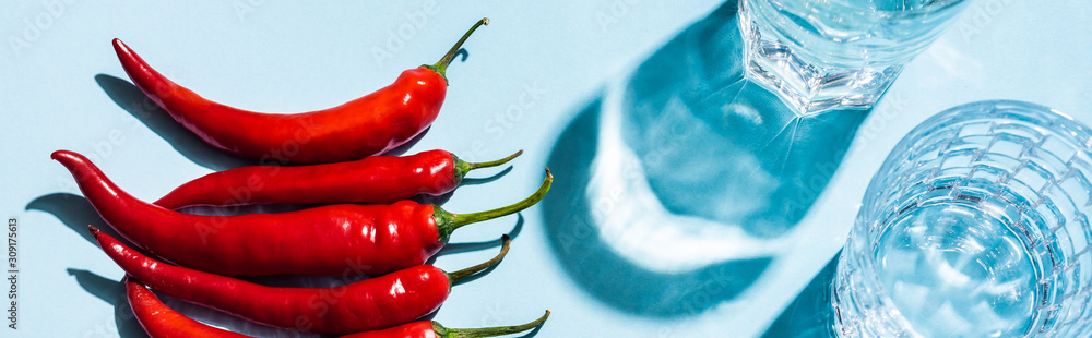 Top view of ripe chili peppers beside glasses of water on blue surface, panoramic shot Top view of ripe chili peppers beside glasses of water on blue surface, panoramic shot