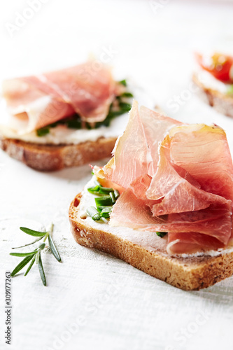 Tasty sandwiches with cream cheese, smoked ham and fresh herbs. Bright wooden background. Close up. 