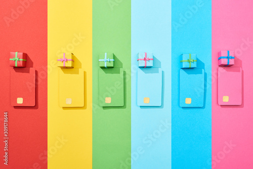 top view of multicolored empty credit cards and gift boxes on rainbow background