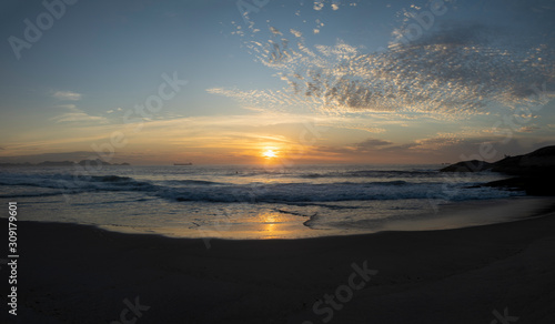 Wide panorama of waves coming in at the Arpoador Devil s beach in Rio de Janeiro  Brazil  at sunrise with the sun reflecting in the water that hits the pristine sand beach