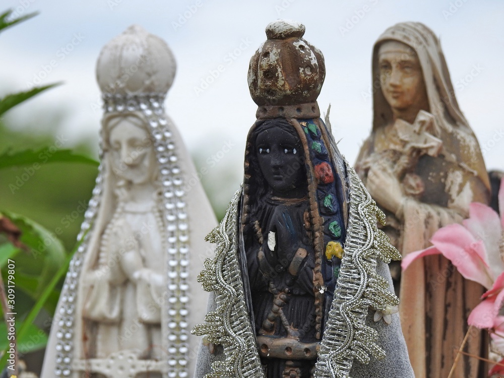 Obraz premium Scene in a cemetery: close-up of a statue of Our Lady of Aparecida, patroness of Brazil, with clasped hands and a crown on her head. It is the black version of the Virgin Mary.