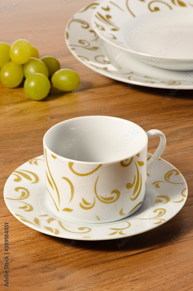 Coffee cup set with saucer on a wooden table with set of dishes in the background Coffee cup set with saucer on a wooden table with set of dishes in the background