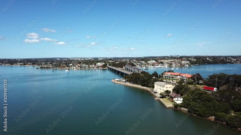 Aerial: Drone flying over water towards a bridge to slowly reveal traffic driving over in Sydney, NSW Aerial: Drone flying over water towards a bridge to slowly reveal traffic driving over in Sydney, NSW
