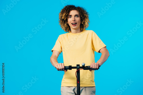 excited curly teenager riding electric scooter isolated on blue © LIGHTFIELD STUDIOS