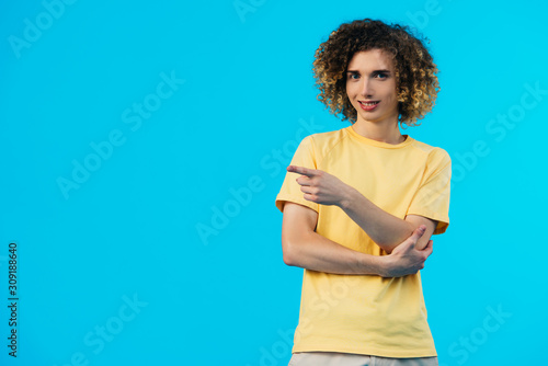 smiling curly teenager pointing with finger isolated on blue