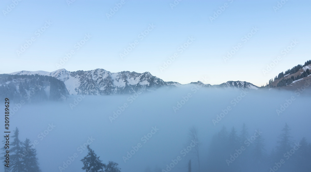 Foggy weather in the Allgau Alps (Bavaria, Germany). Snow-covered mountains in soft light. Copy space