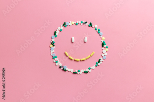 Composition of pills and capsules on a pink background in the form of a smile. Happy emotions. Psychological help. Copy space. View from above. Flat lay.