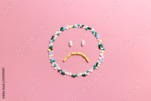 Composition of pills and capsules on a pink background in the form of emoji. Sad emotions. Psychological help. Copy space. View from above. Flat lay.