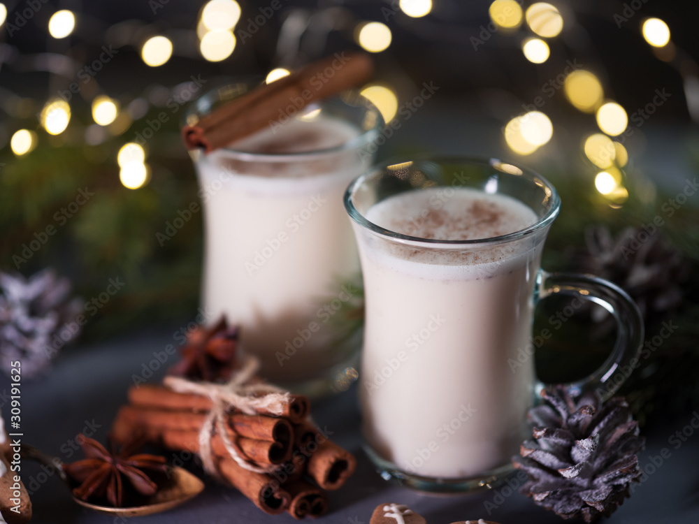 Traditional hot winter and Christmas drink egg nog with cinnamon in glasses on the table with tree branches Traditional hot winter and Christmas drink egg nog with cinnamon in glasses on the table with tree branches