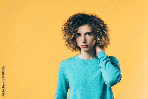 curly teenager touching neck isolated on yellow