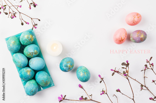 Happy easter card. Stylish minimalistic composition of turquoise with gold easter eggs on a white background. Candles and delicate spring flowers. Flat lay, top view, copy space.