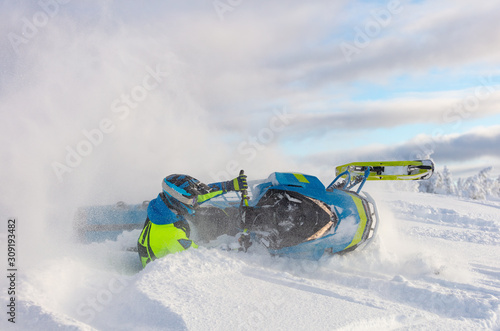 Pro snowmobiler makes a turn and lets a flurry of snow spray from under the caterpillar. a snowmobile with a rider in the turn lying in deep snow. bright skidoo motorbike and suit without brands photo