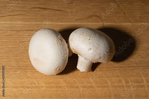 Several whole champignon mushrooms lie on a wooden table. Hard light and contrasting shadows.