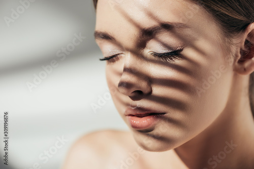 Fotobehang Portrait of nude girl with closed eyes and shadows on face on grey