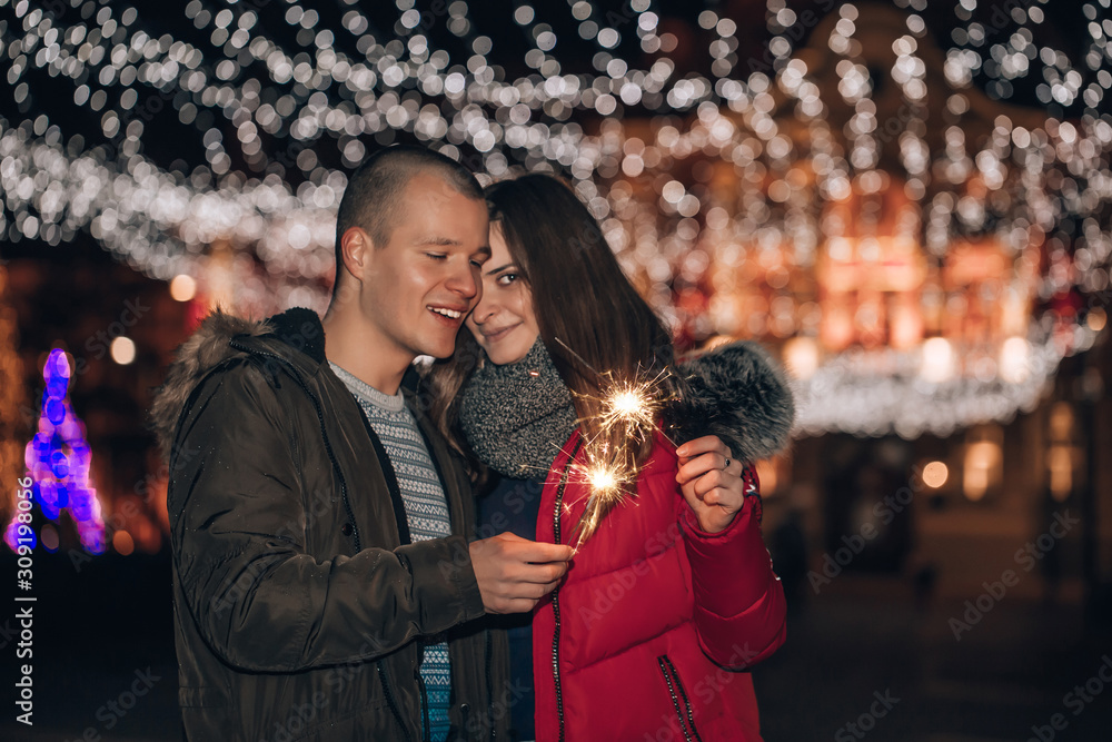 Young happy couple is having fun with sparklers in winter city night Young happy couple is having fun with sparklers in winter city night