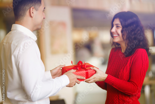 Man giving a christmas present to his girlfriend. Cheerful couple with gift in hands enjoying together on Christmas eve. Winter holidays concept. Lovers give each other gifts. Valentine's Day concept. photo