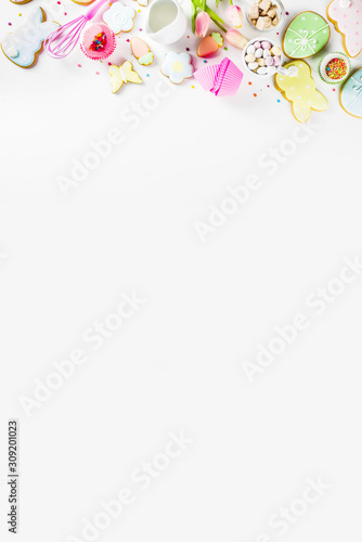Sweet Easter baking cooking background with traditional Easter bunny and egg cookies, sugar sprinkles, ingredients, utensils. White table background copy space layout