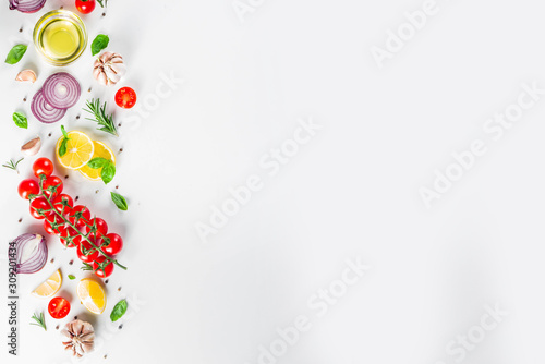Cooking background with spices  vegetables and herbs fresh basil  rosemary  tomato  garlic  onions  lemon on a white kitchen table. Layout top view copy space. Healthy ingredients for cooking
