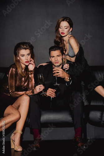 attractive women and handsome man holding champagne glasses isolated on black