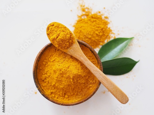 Above of Turmeric powder in spoon and wooden bowl isolated on white background.