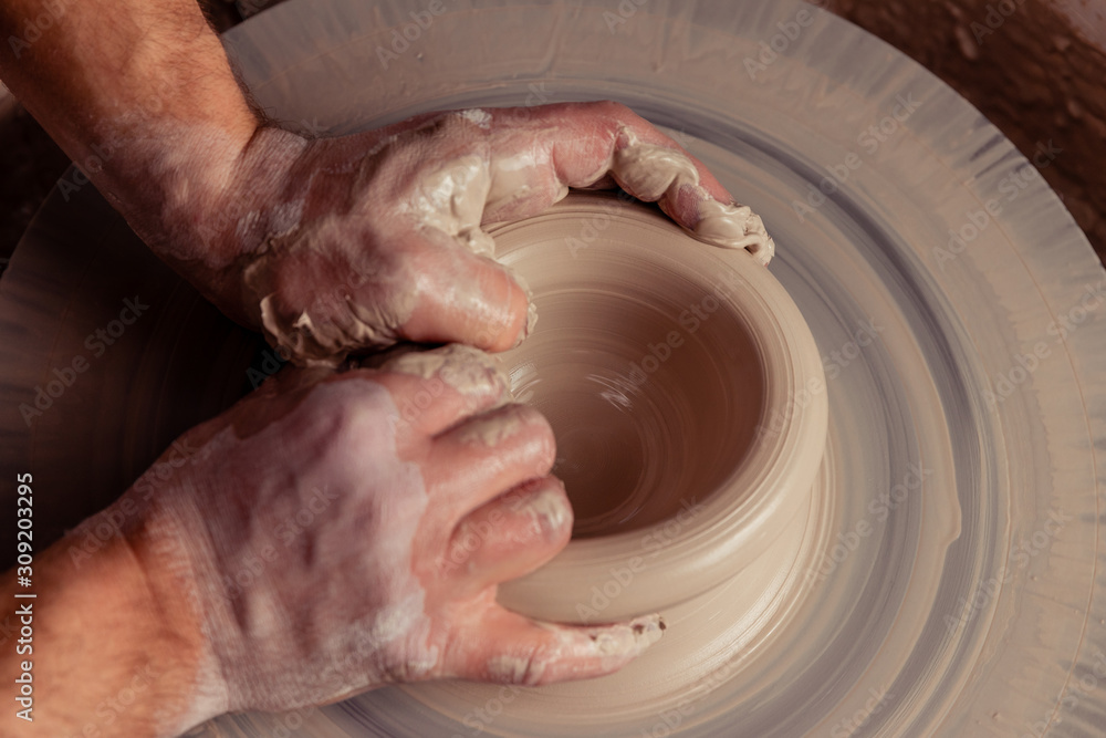 close-up view on dirty man hands of potter creating with fingers and pressure an earthen jar pot of white clay on the potter's wheel circle in studio close-up view on dirty man hands of potter creating with fingers and pressure an earthen jar pot of white clay on the potter's wheel circle in studio