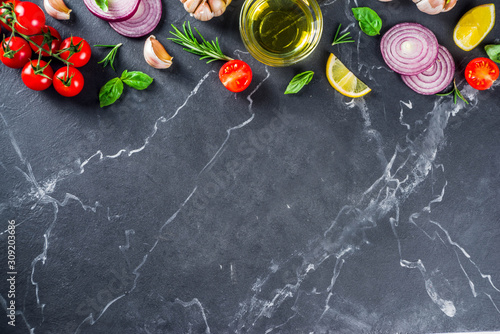 Cooking background with spices, vegetables and herbs fresh basil, rosemary, tomato, garlic, onions, lemon on a black kitchen table. Layout top view copy space. Healthy ingredients for cooking