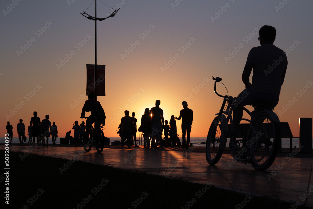 Cyclist silhouette on sea beach crowded sunset background