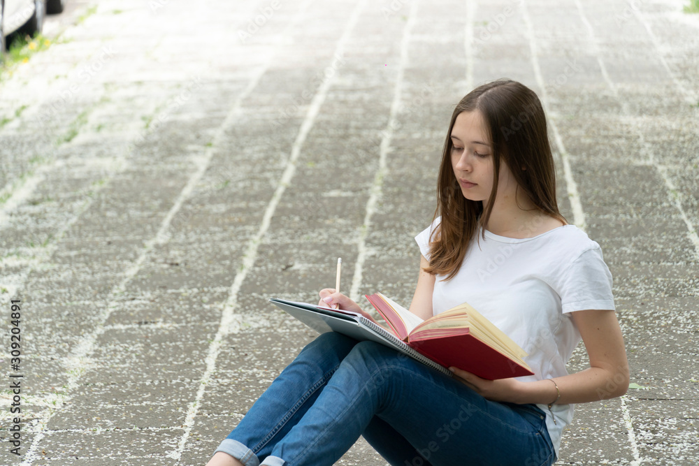 Fototapeta premium Teenage girl studying sitting on the walkway, outdoors