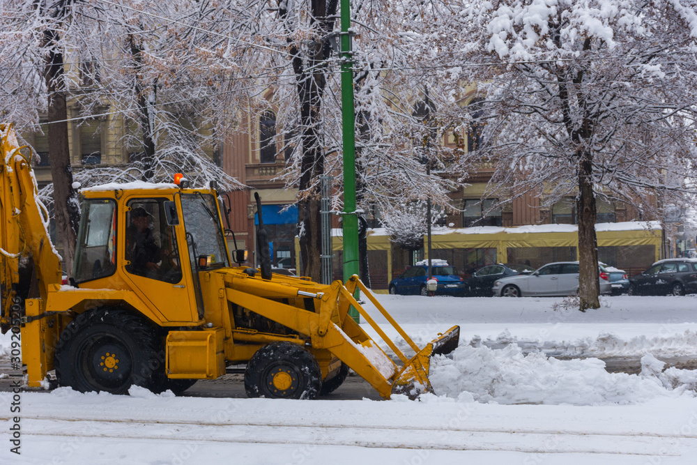 Yellow tractor with snowplow removing snow from the streets. 